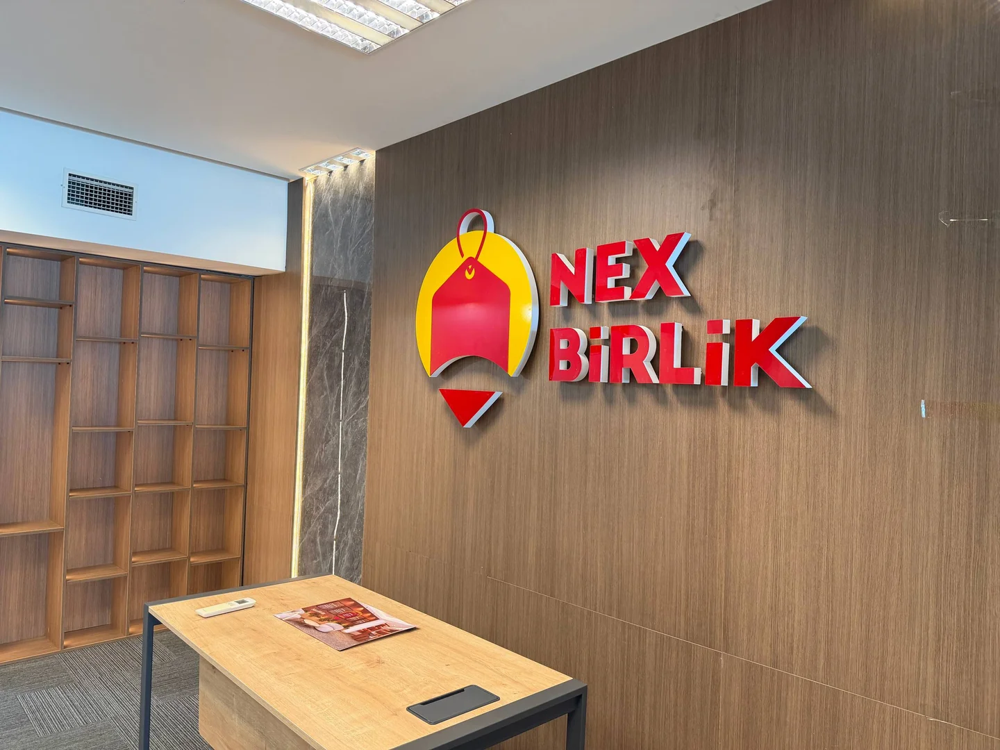 NexBirlik loqosu və masa olan boş qəbul sahəsi